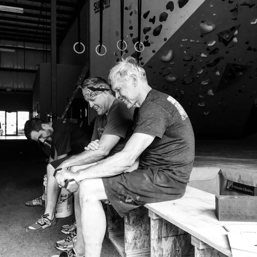 Group of men sitting on a bench in the climbing gym doing wrist curls